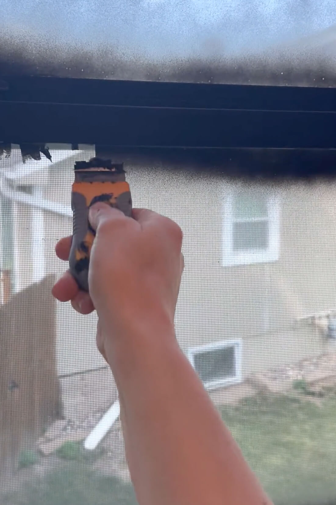 Scraping paint off of the window using a razor blade.